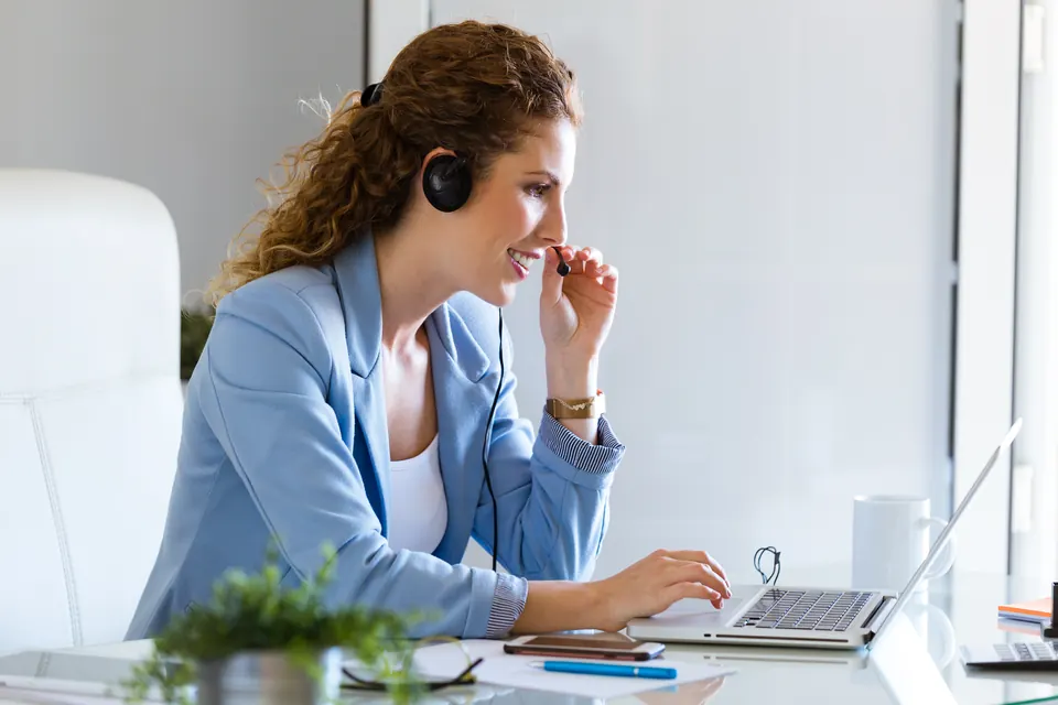 Assistante avec casque-micro gérant un appel devant son ordinateur portable