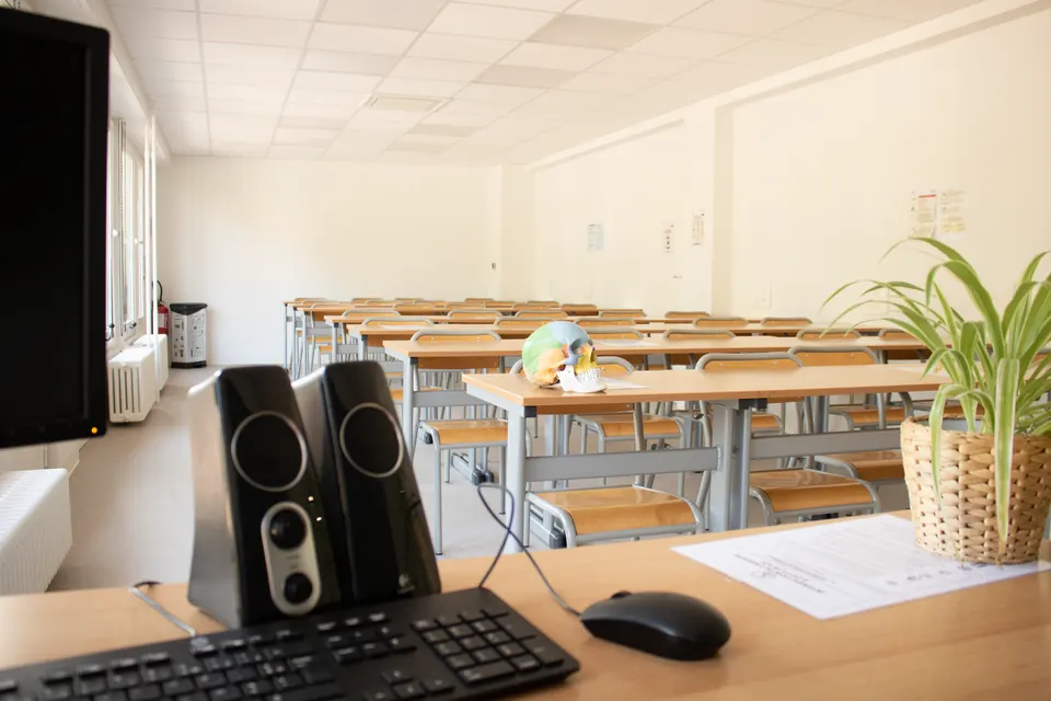 Poste informatique au premier plan dans une salle de cours d'Exactétudes