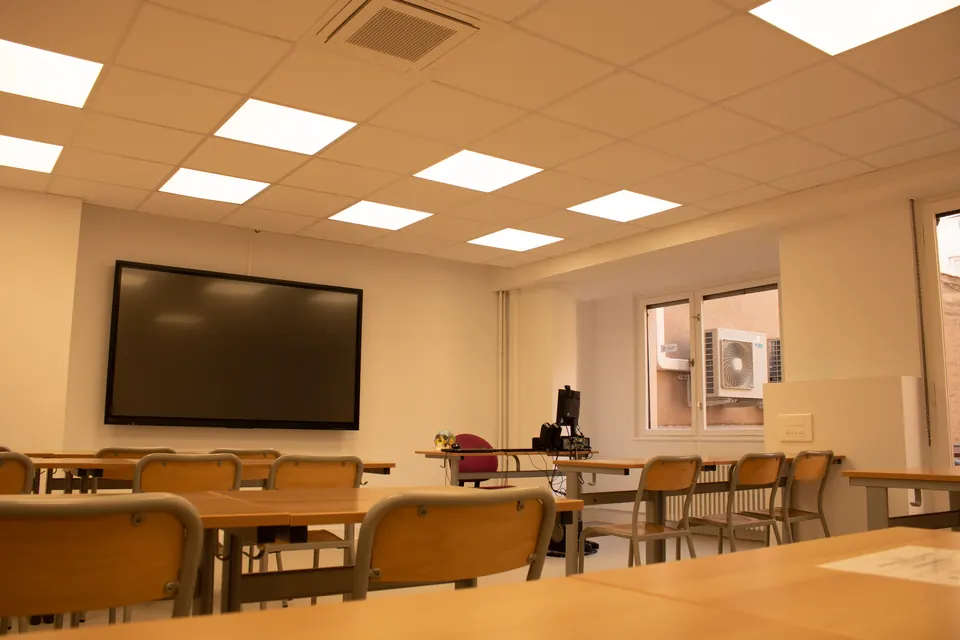 Salle de cours avec tables alignées face à un grand écran interactif